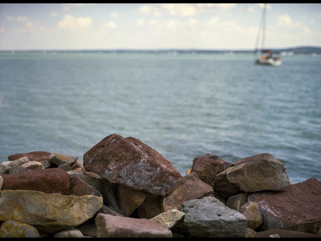 Rocky shoreline of Lake Balaton in Hungary with a sailing boat on calm blue water